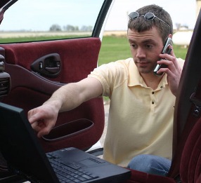 Мужчина возле автомобиля с ноутбуком говорит по мобильному телефону